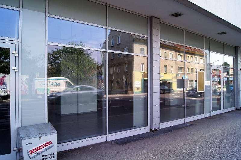 Fassade eines Geschäftsgebäudes mit großen Schaufenstern, die die Straße und gegenüberliegende Gebäude widerspiegeln.
