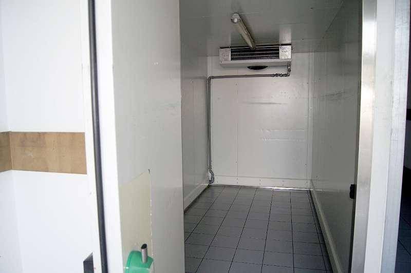 Innenansicht eines kleinen, gefliesten Kühlraums mit Lüftungseinheit an der Decke und einfachen Wänden.