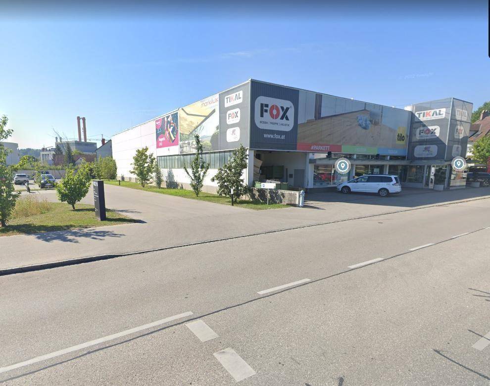 Außenansicht eines modernen Geschäftsgebäudes mit großen Werbeschildern und Parkplätzen davor.