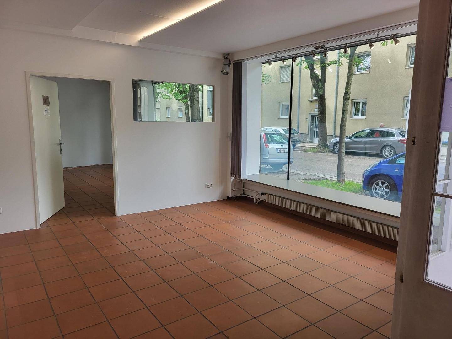 Geräumiger, leerer Geschäftsraum mit Terrakotta-Fliesenboden und großen Schaufenstern zur Straße.