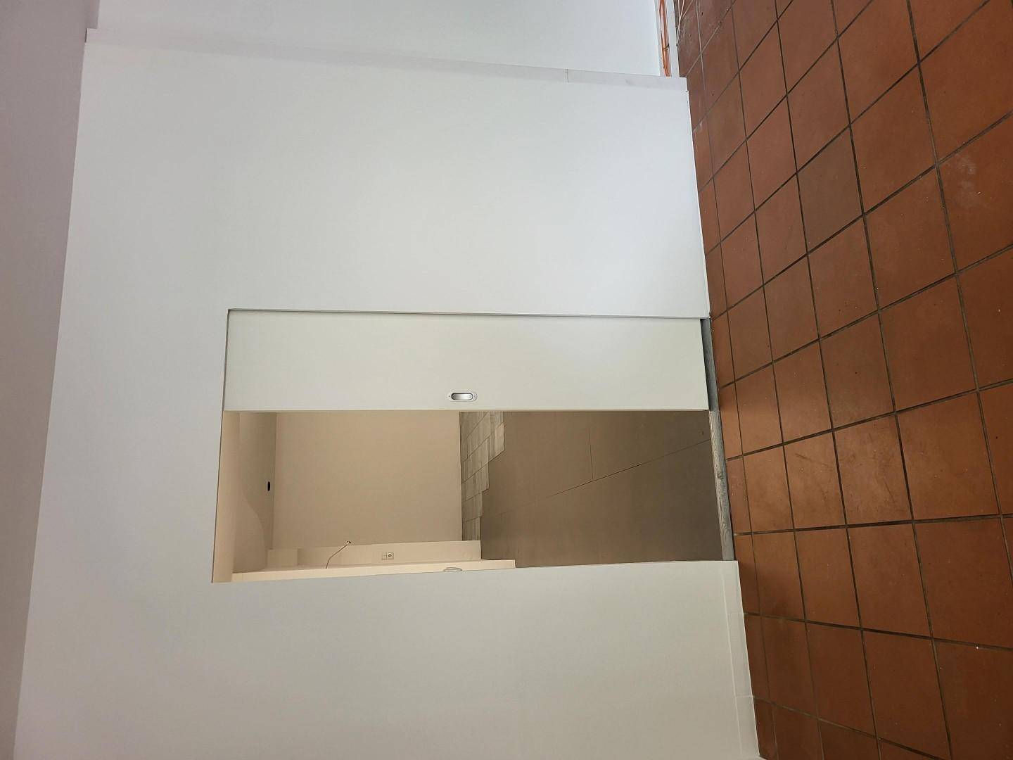 Blick von oben auf eine Treppe mit Terrakotta-Fliesenboden und weißen Wänden.
