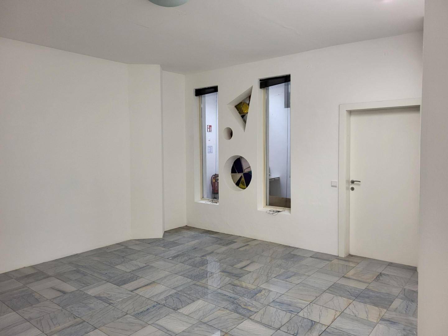 Heller Raum mit grauen Marmorfliesen, weißen Wänden und dekorativen Fensterausschnitten.