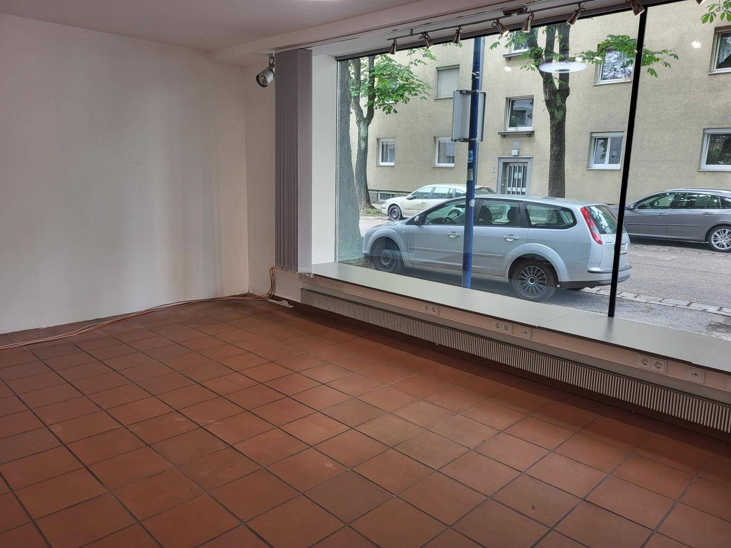 Leerer Geschäftsraum mit Terrakotta-Fliesenboden und breiten Schaufenstern mit Blick auf die Straße.