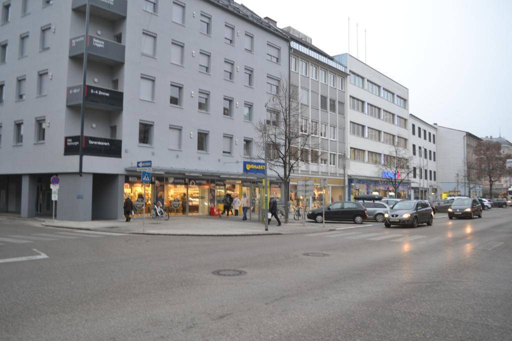 Straßenansicht einer belebten Kreuzung mit Geschäftsgebäuden und fließendem Verkehr.