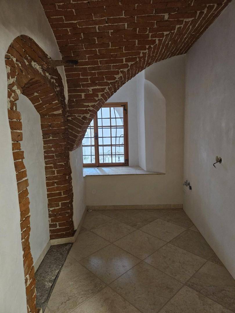 Kleiner Innenraum mit Ziegelgewölbe, einem Fenster und gefliestem Boden, möglicherweise für eine Küche vorbereitet.