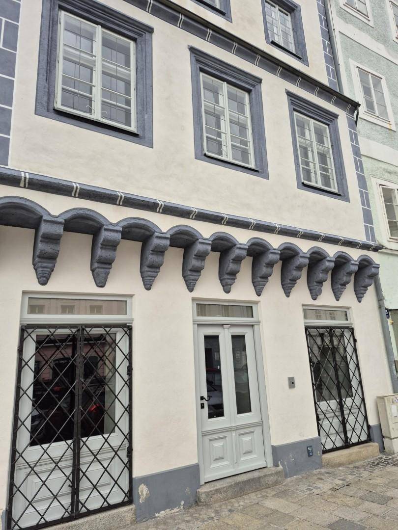 Historische Gebäudefassade mit dekorativen Konsolen, großen Fenstern und Eingangstüren im Erdgeschoss.
