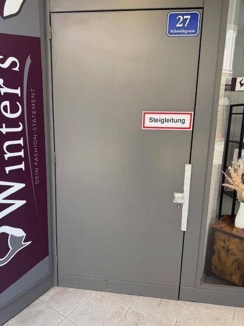Graue Eingangstür mit Hausnummer und Hinweisschild "Steigleitung" an einem Geschäftsgebäude.