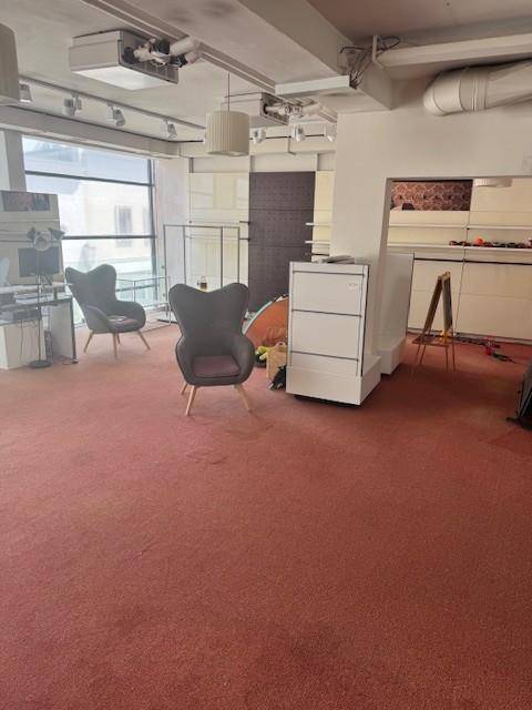 Offener Lounge-Bereich mit rotem Teppichboden, bequemen Sesseln und großen Fenstern mit Stadtblick.
