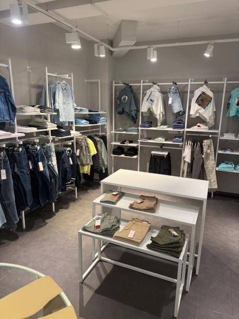 Heller Verkaufsbereich mit verschiedenen Kleiderständern und Auslagen für Bekleidung auf weißem Hintergrund.