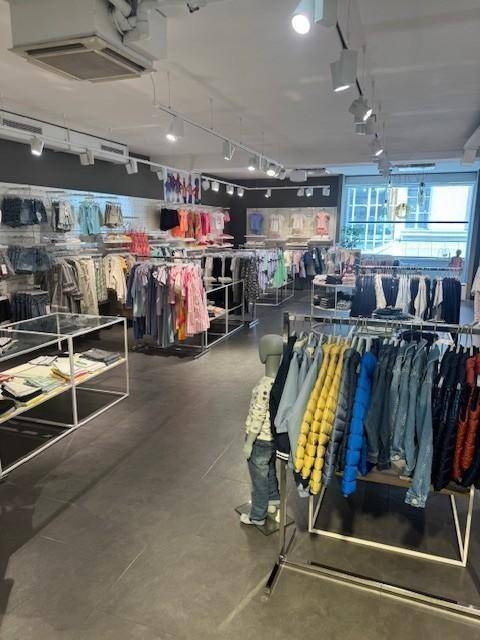 Heller Verkaufsraum eines Bekleidungsgeschäfts mit zahlreichen Kleiderständern und Auslagen auf Fliesenboden.