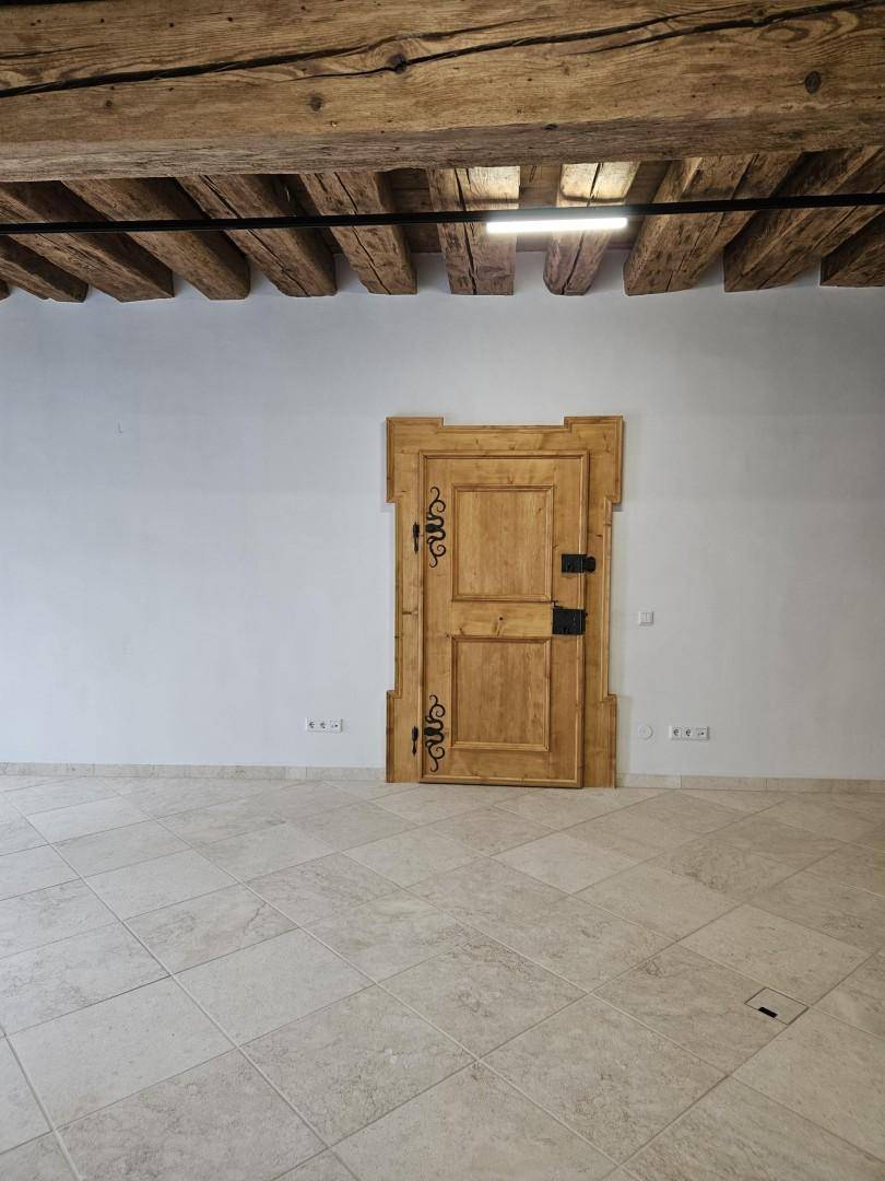 Detailansicht einer kunstvoll geschnitzten Holztür mit schmiedeeisernen Beschlägen in einem hellen Raum.