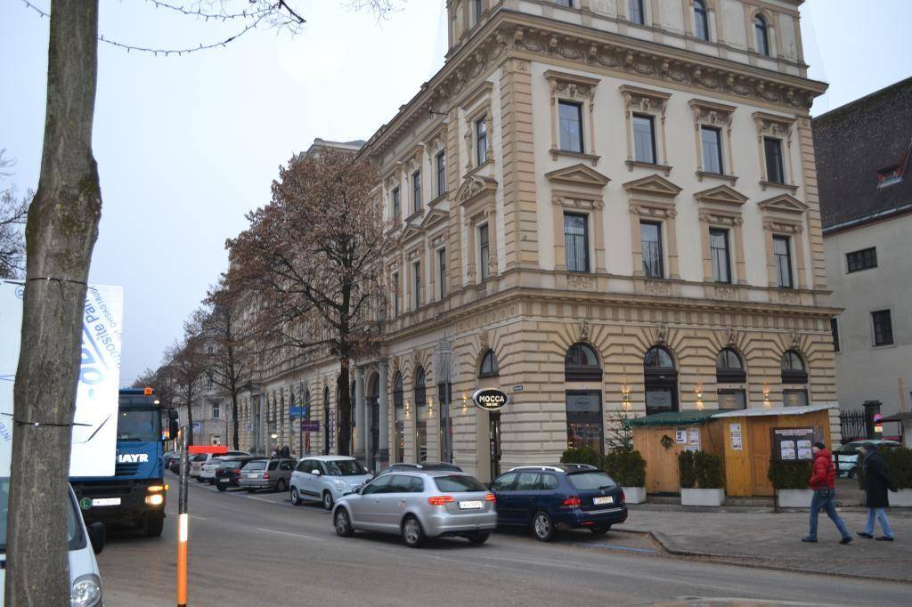 Historisches Gebäude mit aufwendiger Fassade entlang einer Straße mit parkenden Fahrzeugen.