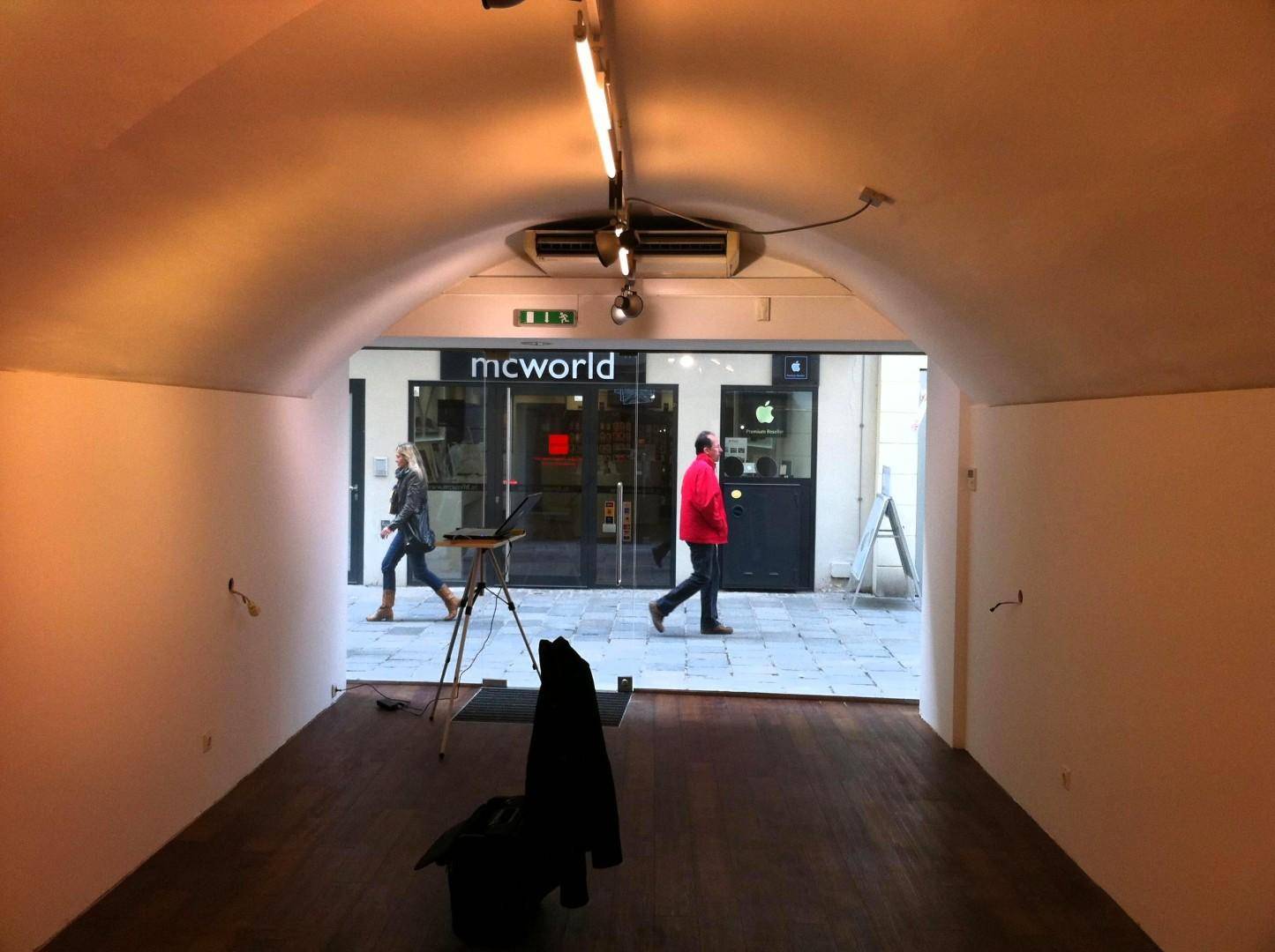 Blick aus dem leeren Verkaufsraum zur Straße, mit Passanten und angrenzenden Geschäften durch die Glasfront sichtbar.