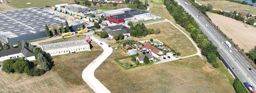 Panoramische Luftaufnahme eines Gewerbegebiets mit Autobahn, großen Hallen und landwirtschaftlichen Flächen.