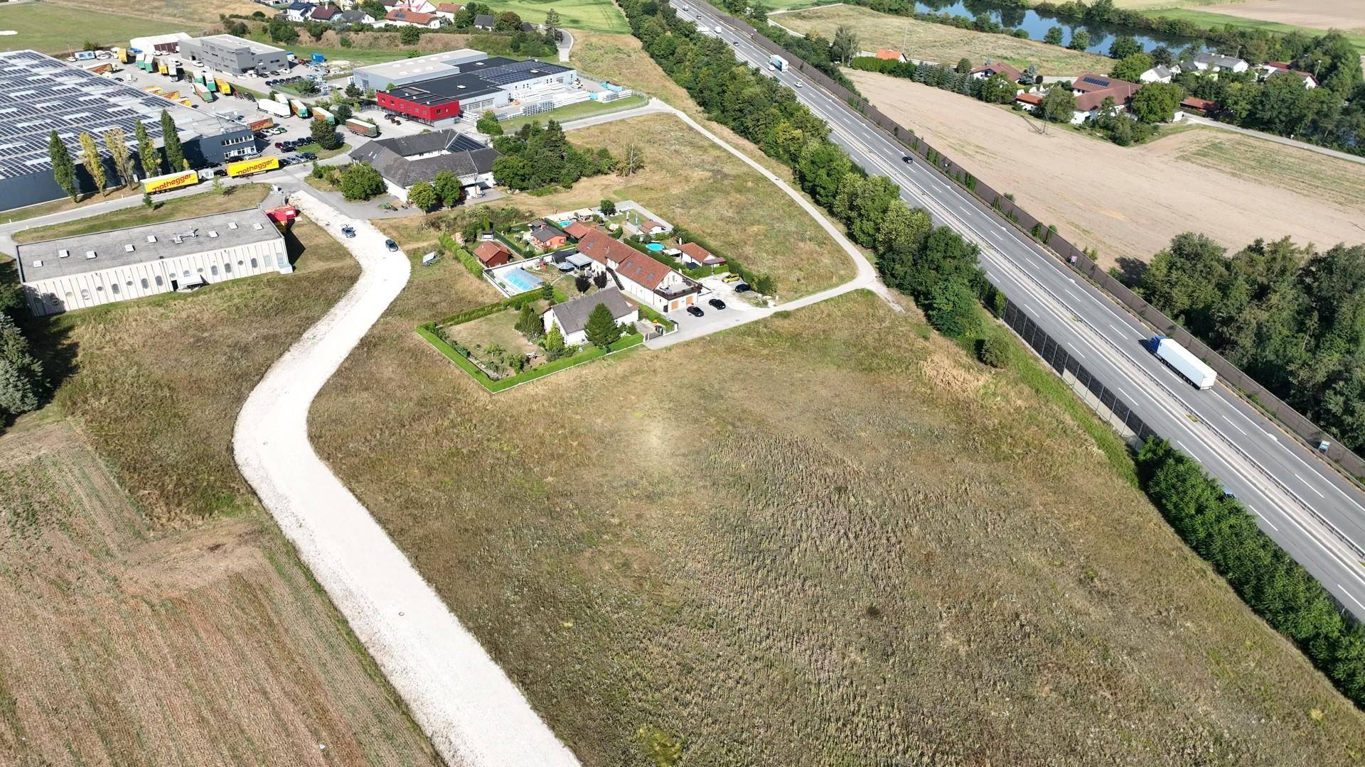 Weitläufige Luftaufnahme eines Gewerbegebiets mit angrenzender Autobahn, Feldern und einzelnen Wohnhäusern.