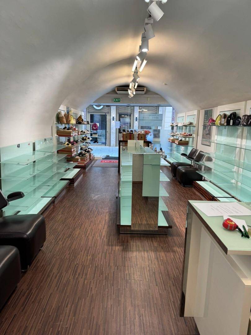 Langer Verkaufsraum eines Schuhgeschäfts mit gewölbter Decke, Regalen und Blick zum Eingangsbereich.