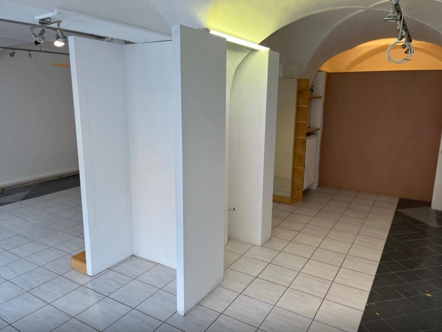 Innenansicht eines Ladenraums mit gewölbter Decke, Fliesenboden und einer teilweise farbigen Wand.