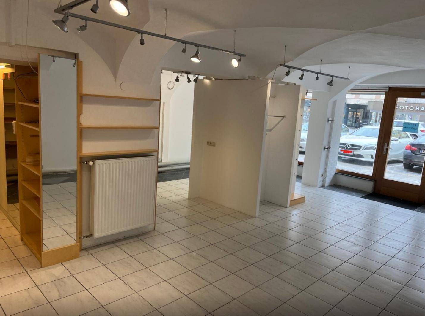 Heller Ladenraum mit gewölbter Decke, Fliesenboden und Blick auf die Straße durch große Fenster.