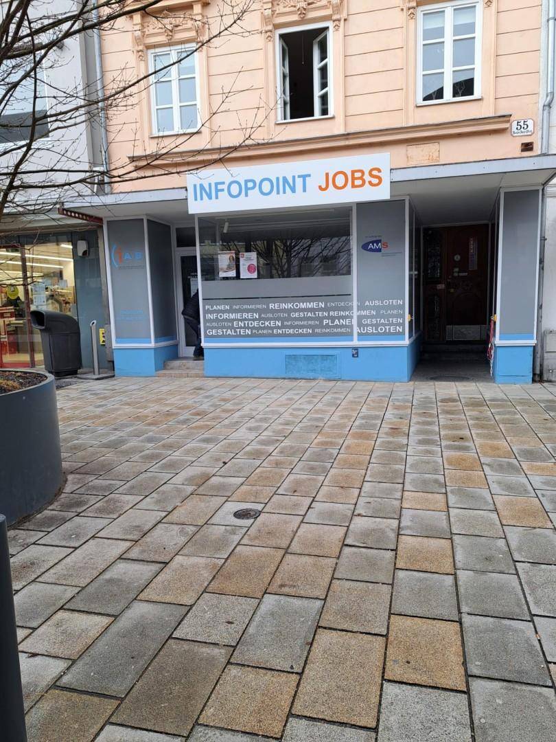Außenansicht eines Geschäftsgebäudes mit "Infopoint Jobs" Beschriftung und gepflastertem Vorplatz, modern gestaltet.