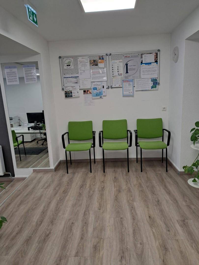 Wartebereich mit drei grünen Stühlen, einer Pinnwand und hellem Laminatboden, schlicht und funktional.