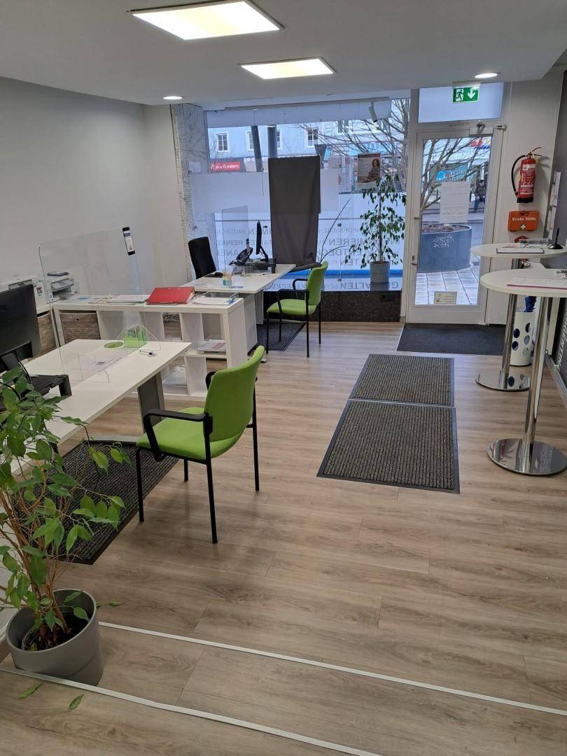 Helles Büro mit mehreren Arbeitsplätzen, grünen Stühlen und großer Fensterfront zur Straße.