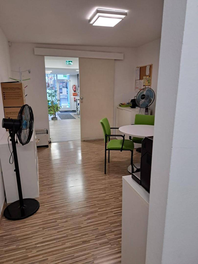 Flur mit Schiebetür, Blick in den Empfangsbereich und einem kleinen Besprechungstisch, funktional gestaltet.