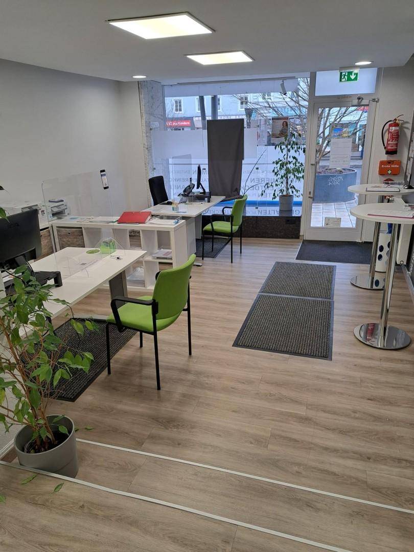 Modernes Büro mit Arbeitsplätzen, grünen Stühlen und großer Glasfront zur Straße hin.