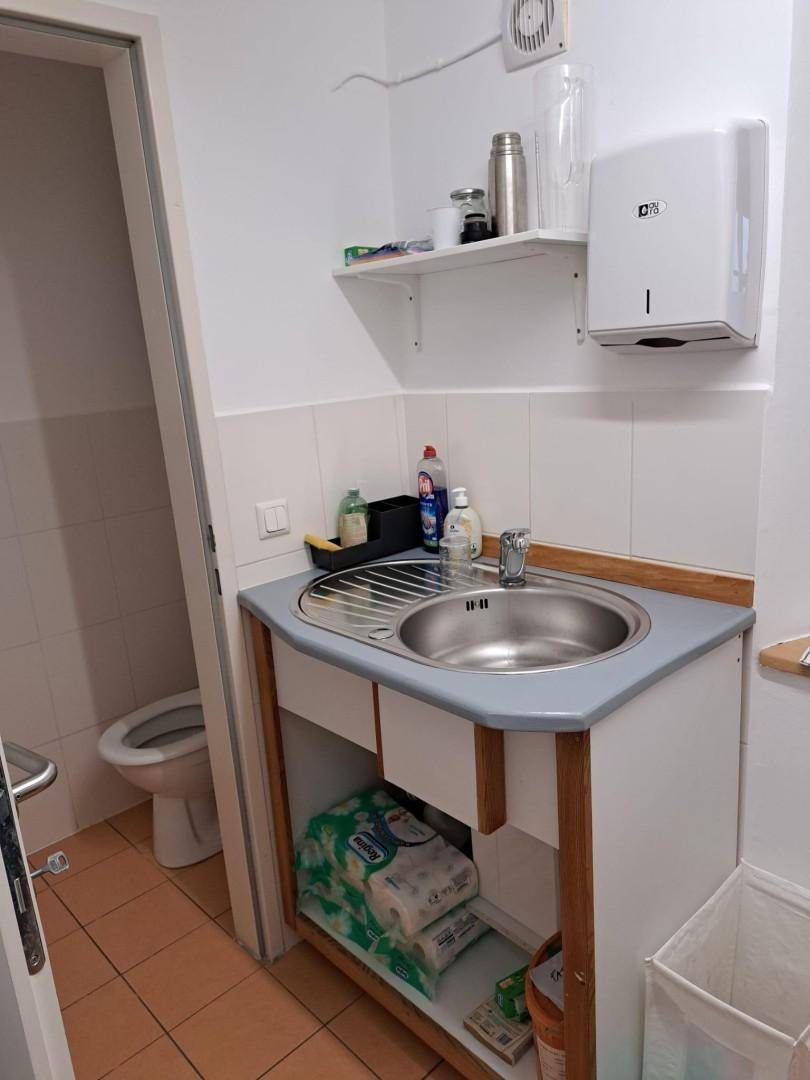 Kleine Küchenzeile mit Spülbecken, Regal und Zugang zu einer Toilette, praktisch eingerichtet.