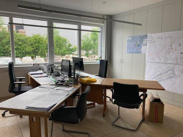 Geräumiges Büro mit mehreren Arbeitsplätzen, Computern und großen Fenstern mit Blick ins Grüne.