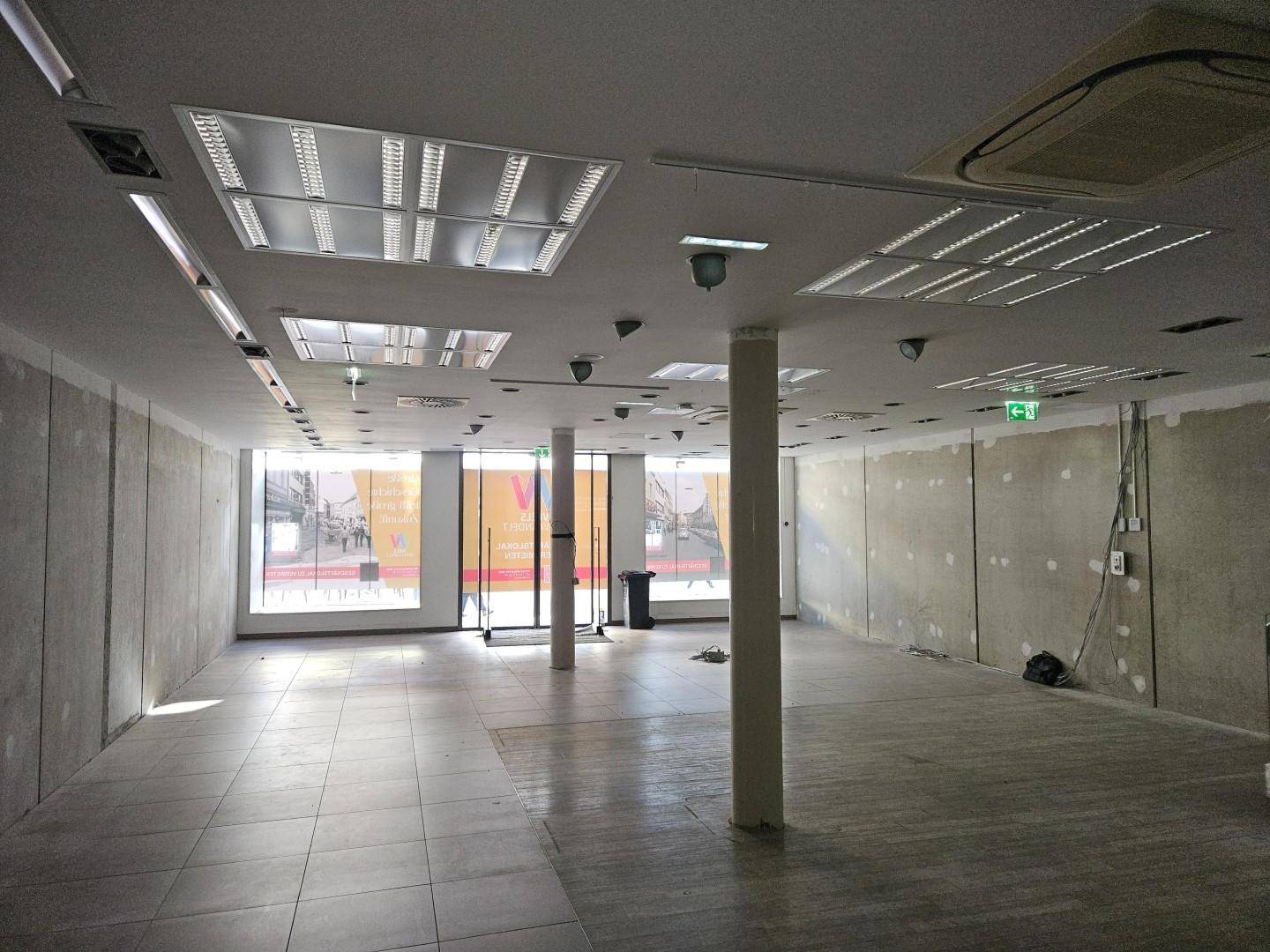 Großer, leerer Gewerberaum mit Fliesenboden, Säulen und Deckenbeleuchtung.