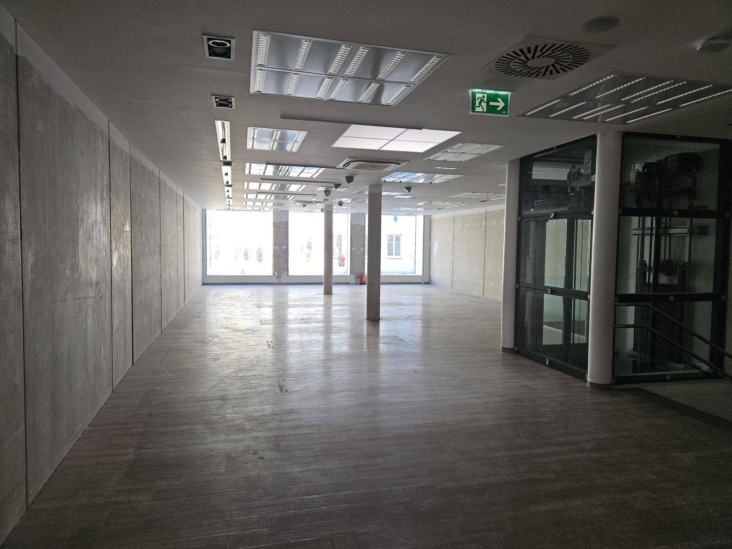 Geräumiger Gewerberaum mit modernem Bodenbelag, Glasaufzug und großen Fenstern zur Straße.