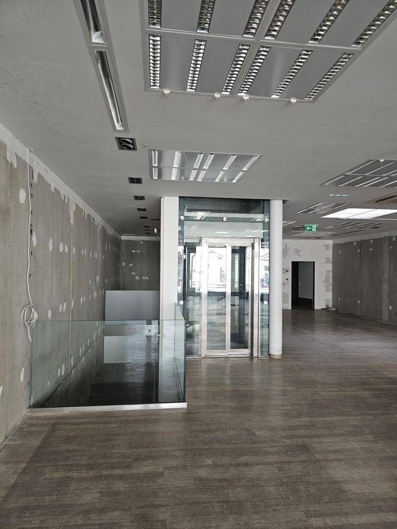 Geräumiger Gewerberaum mit Holzoptik-Boden, Glasgeländer und einem modernen Aufzug in der Mitte.
