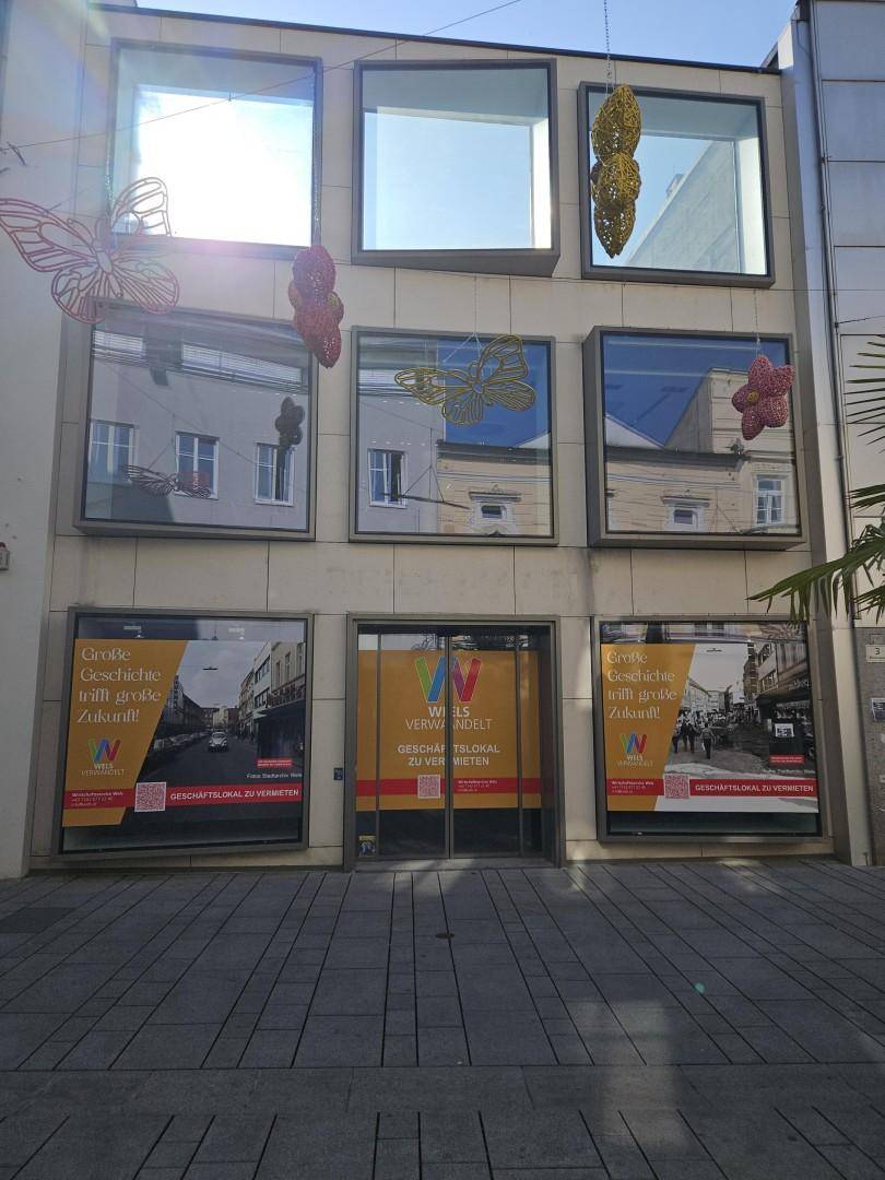 Geschäftsfassade mit großen Schaufenstern, die mit Werbebannern verdeckt sind, und dekorativen Schmetterlingen.