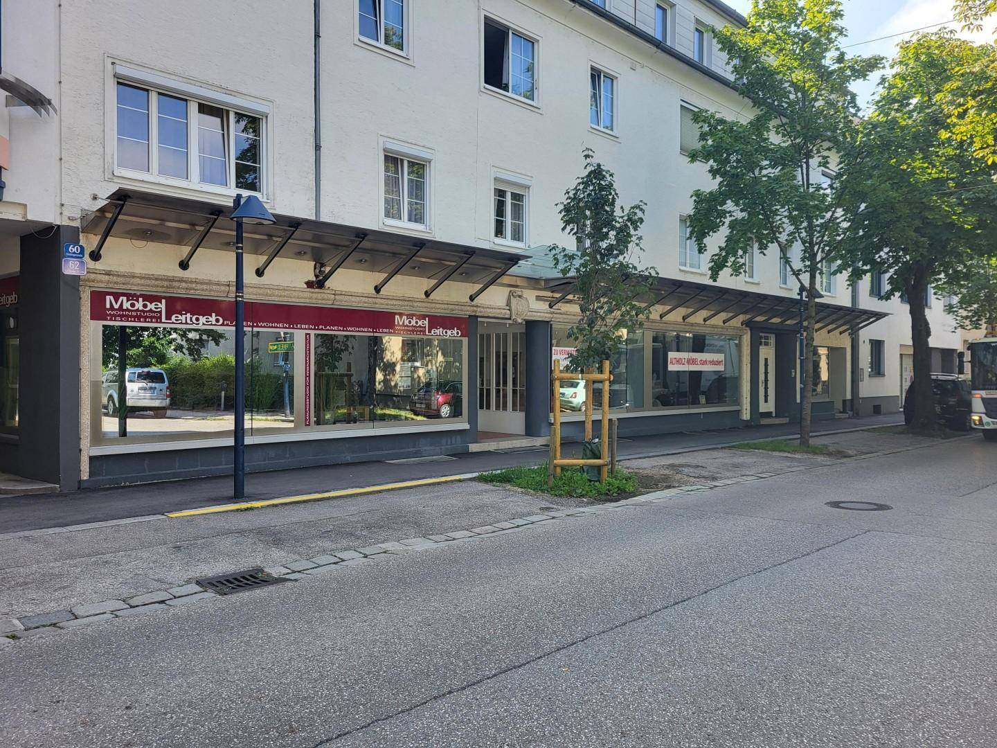 Ansicht der Geschäftsfassade eines Gebäudes mit großen Schaufenstern und Vordach an einer Straße.
