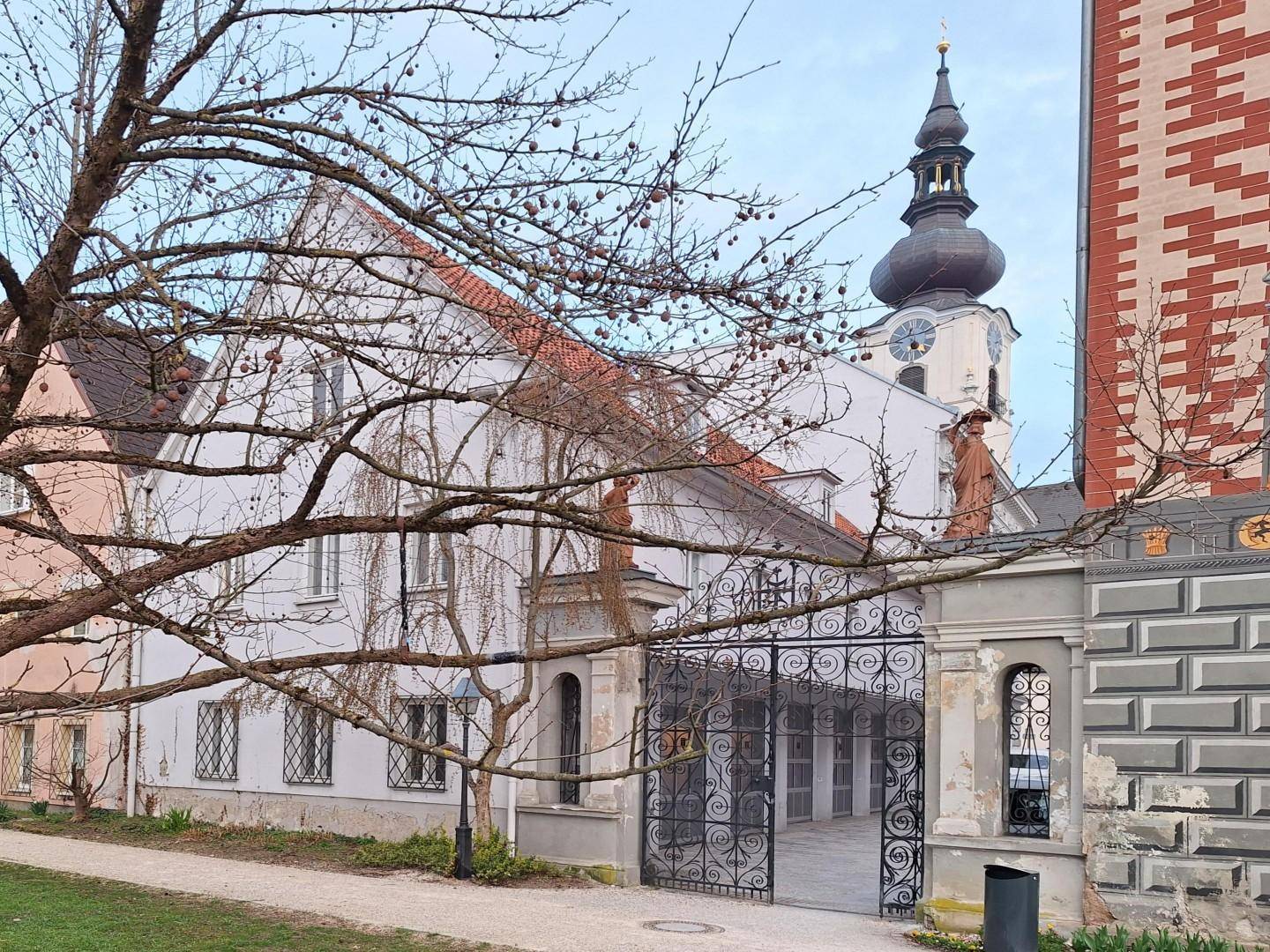 Historisches Gebäude mit Gartenbereich im Vordergrund und einem Kirchturm im Hintergrund.