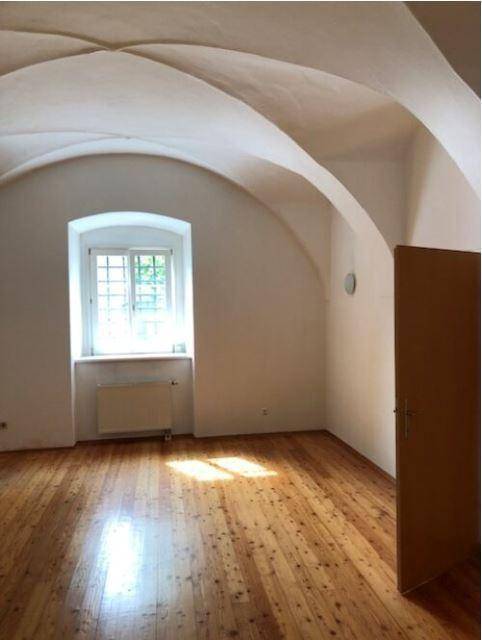 Geräumiger Wohnbereich mit eleganter Gewölbedecke, einem Fenster und glänzendem Holzdielenboden.