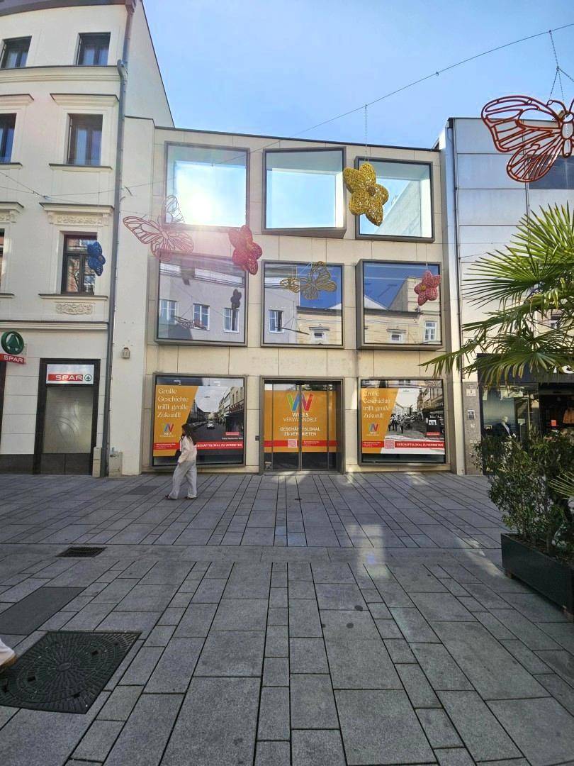 Moderne Geschäftsfassade an einer belebten Fußgängerzone mit großen Schaufenstern und Dekoration.