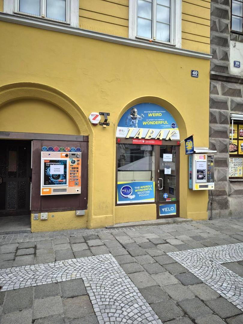 Gelbe Gebäudefassade mit einem Tabakladen im Erdgeschoss und gepflastertem Gehweg davor.