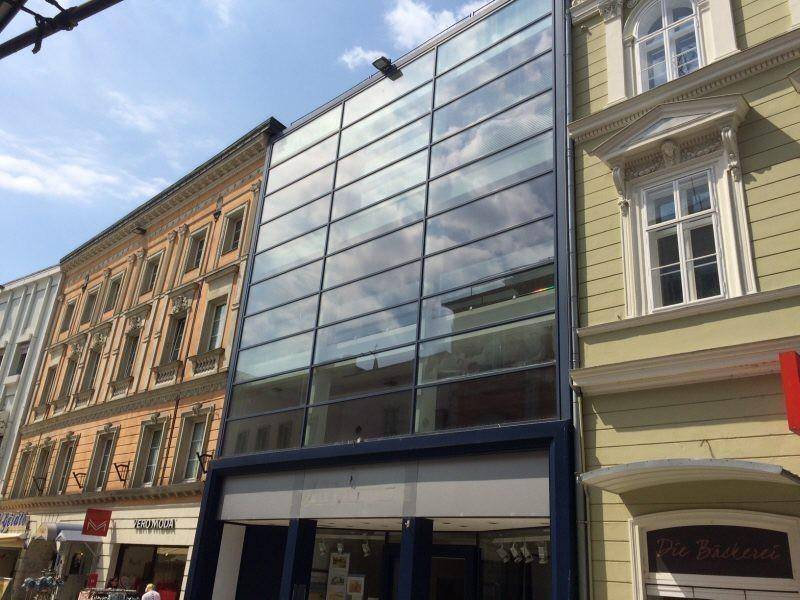 Zeitgenössisches Gebäude mit einer reflektierenden Glasfassade, eingebettet zwischen traditionellen Altbauten.