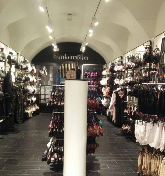 Innenansicht eines Bekleidungsgeschäfts mit gewölbter Decke und dunklem Fliesenboden, präsentiert Unterwäsche.
