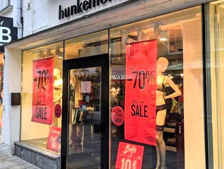 Schaufenster eines Bekleidungsgeschäfts mit großen Glasflächen, Mannequins und roten Sale-Schildern.