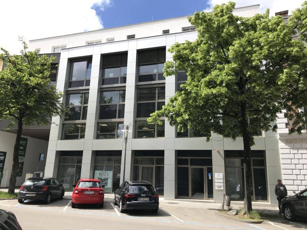 Modernes Geschäftsgebäude mit großen Glasflächen und Parkplätzen, aufgenommen an einem sonnigen Tag.