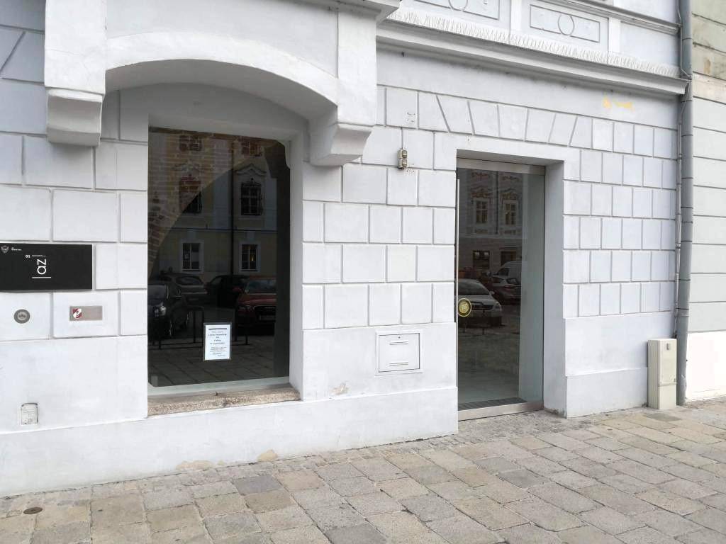 Helle Fassade eines Gebäudes mit großen Fenstern und einer Glastür auf Straßenniveau.