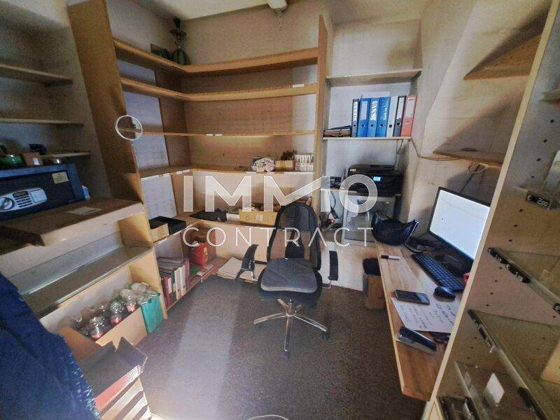 Kleines Büro oder Lagerraum mit vielen Holzregalen, einem Schreibtisch und Bürostuhl.
