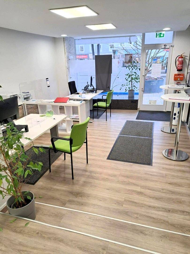 Modernes Büro mit Arbeitsplätzen, grünen Stühlen und großen Fenstern zur Straße.