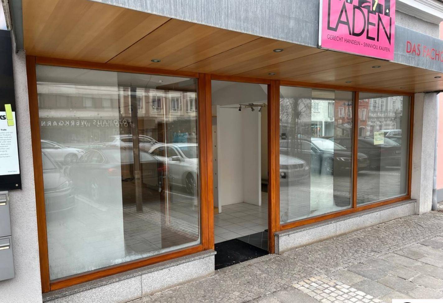 Leere Ladenfront mit großen Schaufenstern und Holzrahmen, die die Straße widerspiegeln.