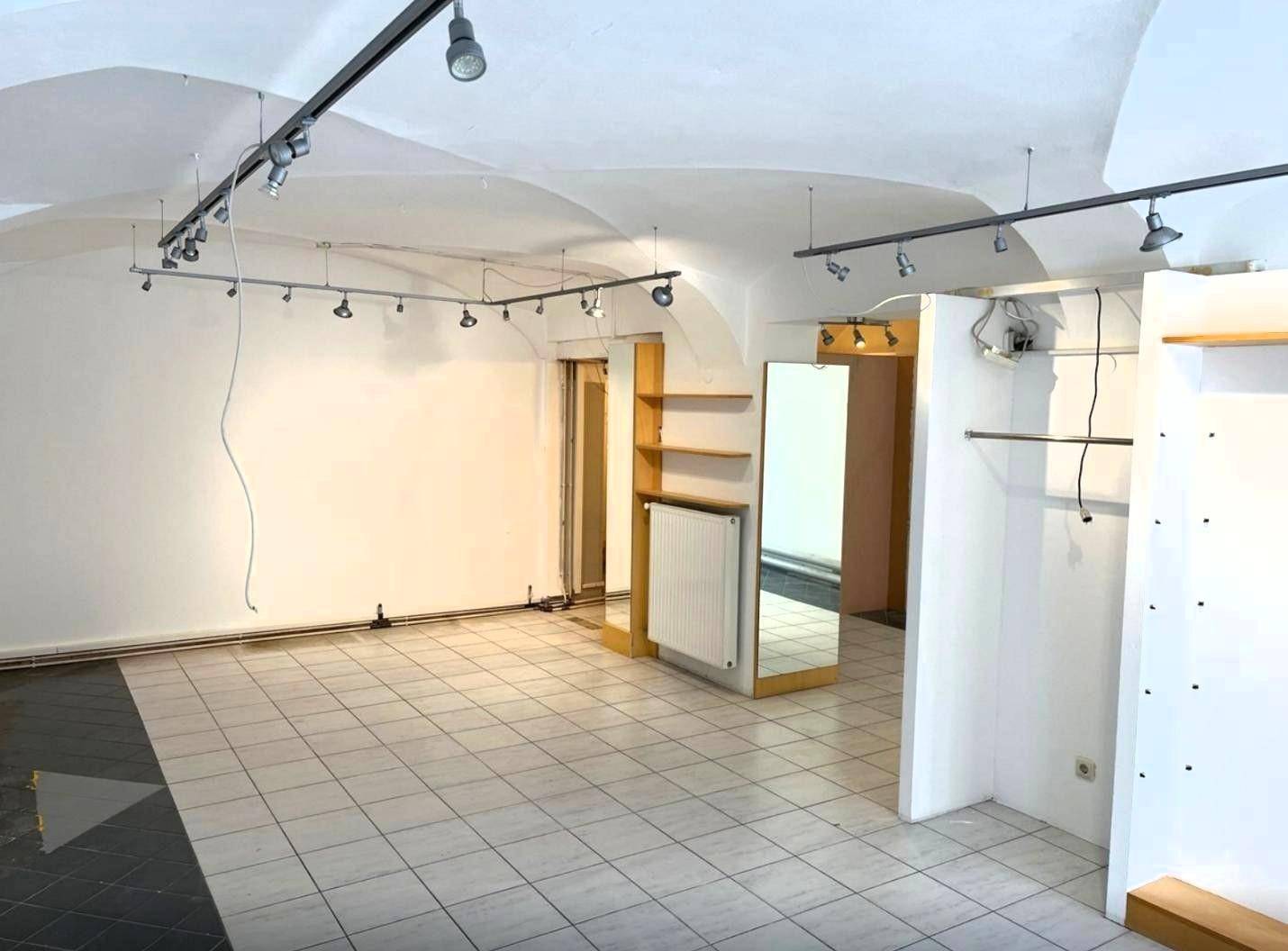 Leerer Ladenraum mit gewölbter Decke, Fliesenboden und Schienensystem für Beleuchtung.