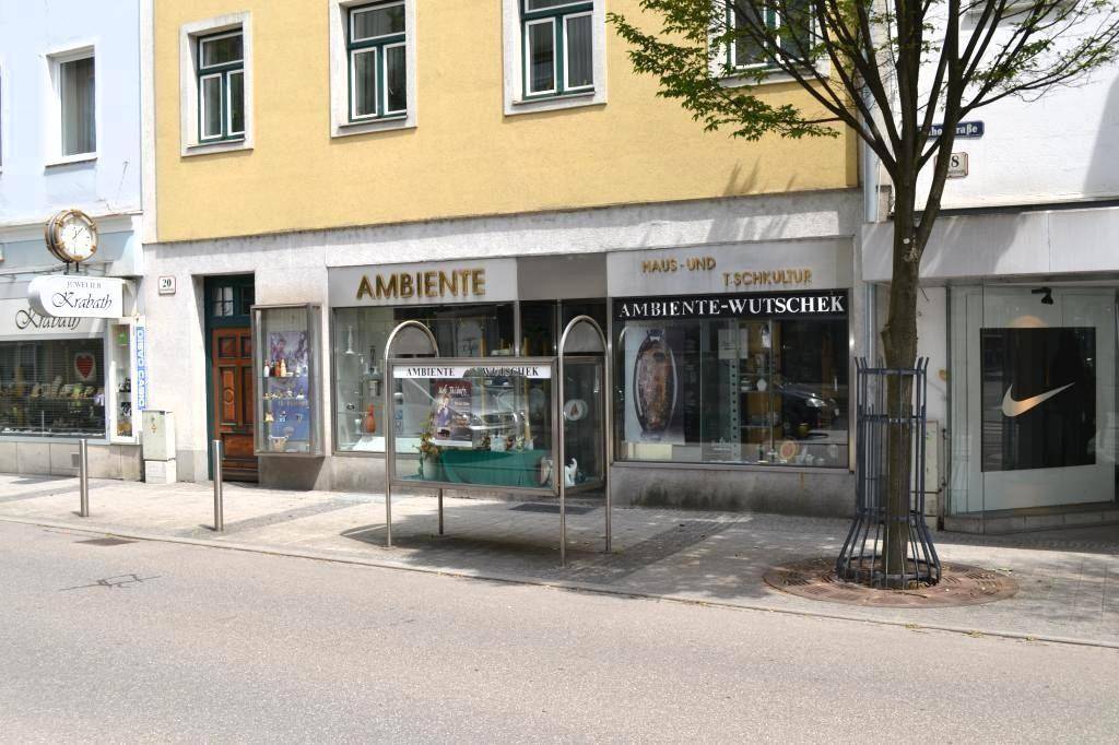 Gelbe Gebäudefassade mit Schaufenstern und einem Baum davor, an einem sonnigen Tag.