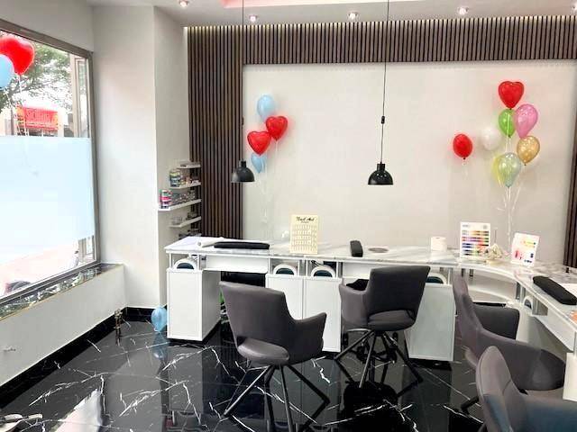 Moderner Nagelstudio-Bereich mit glänzendem schwarzen Marmorboden, weißen Arbeitstischen und festlicher Dekoration.