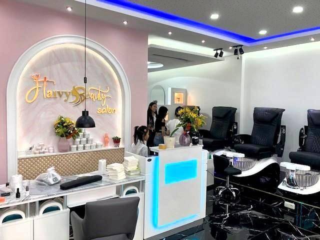 Moderner Schönheitssalon mit Empfangstheke, Pediküre-Stühlen und stilvoller Beleuchtung in Rosa- und Weißtönen.